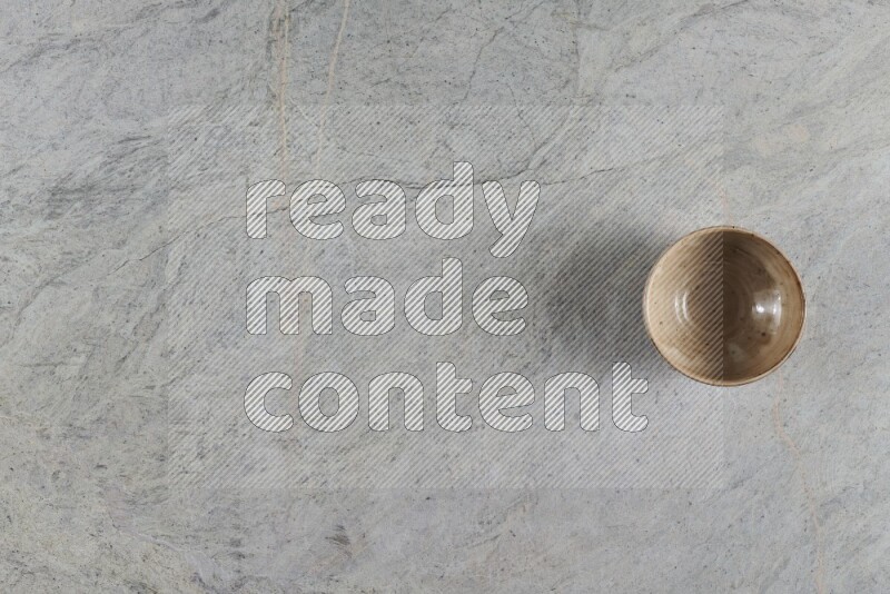A small beige pottery bowl on grey marble background