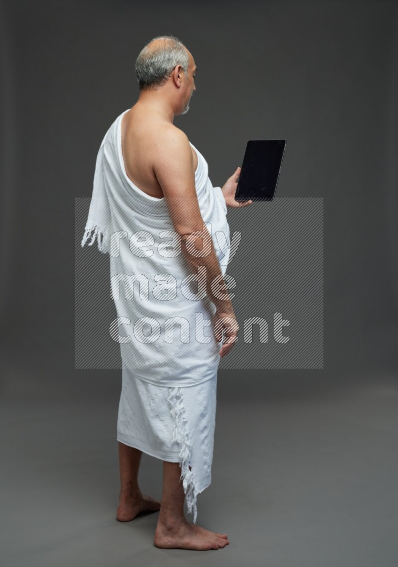 A man wearing Ehram Standing working on tablet on gray background