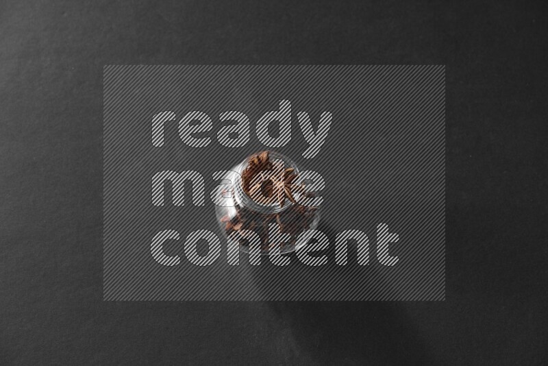 A glass spice jar full of star anise on black flooring