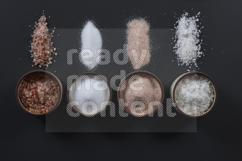 4 pottery bowls filled with himalayan salt and white salt on black background