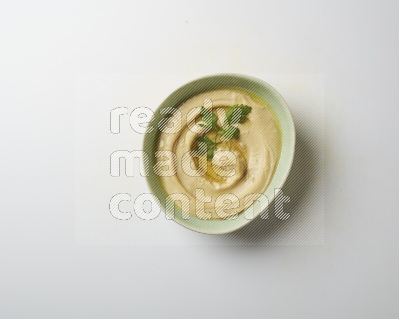Hummus in a green plate garnished with parsley on a white background