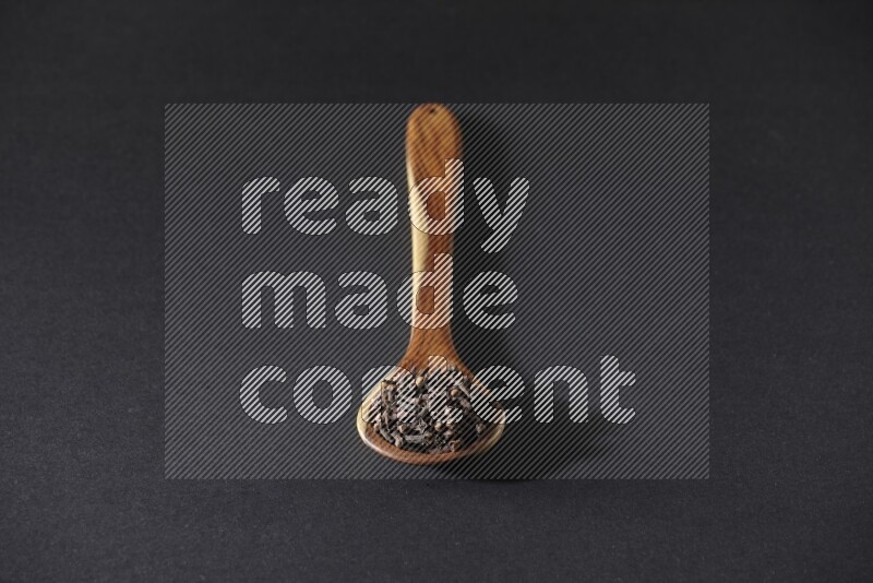 A wooden ladle full of whole cloves on a black flooring