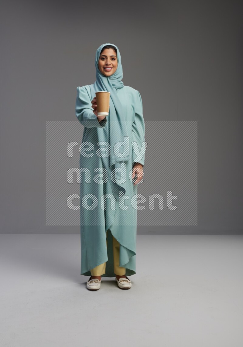 Saudi Woman wearing Abaya standing  holding paper cup on Gray background