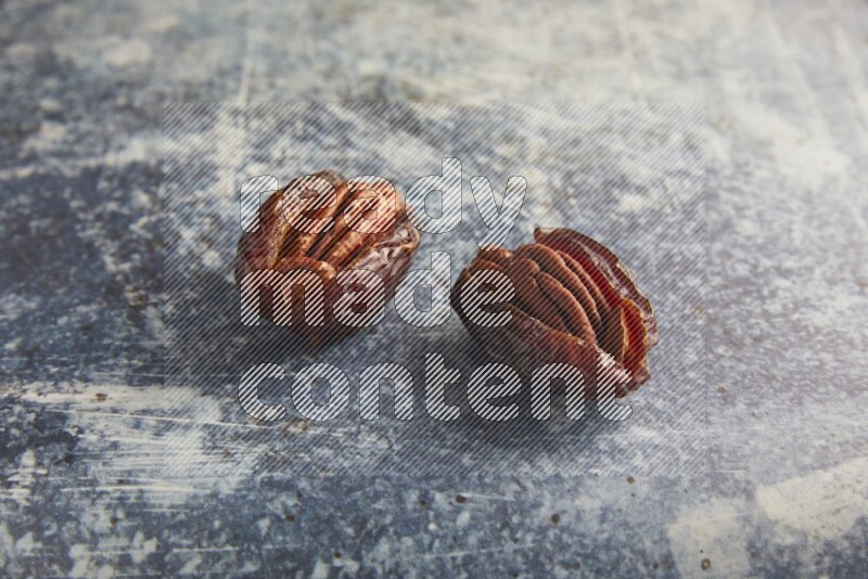 two pecan stuffed madjoul dates on a rustic blue background