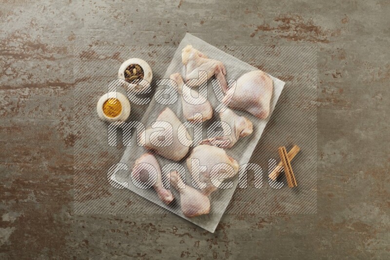 Mixed fresh chicken pieces on a parchment paper direct on a textured rustic background