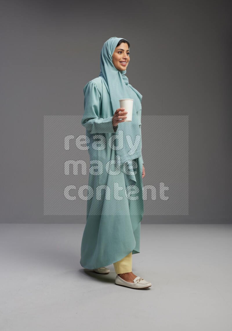 Saudi Woman wearing Abaya standing  holding paper cup on Gray background