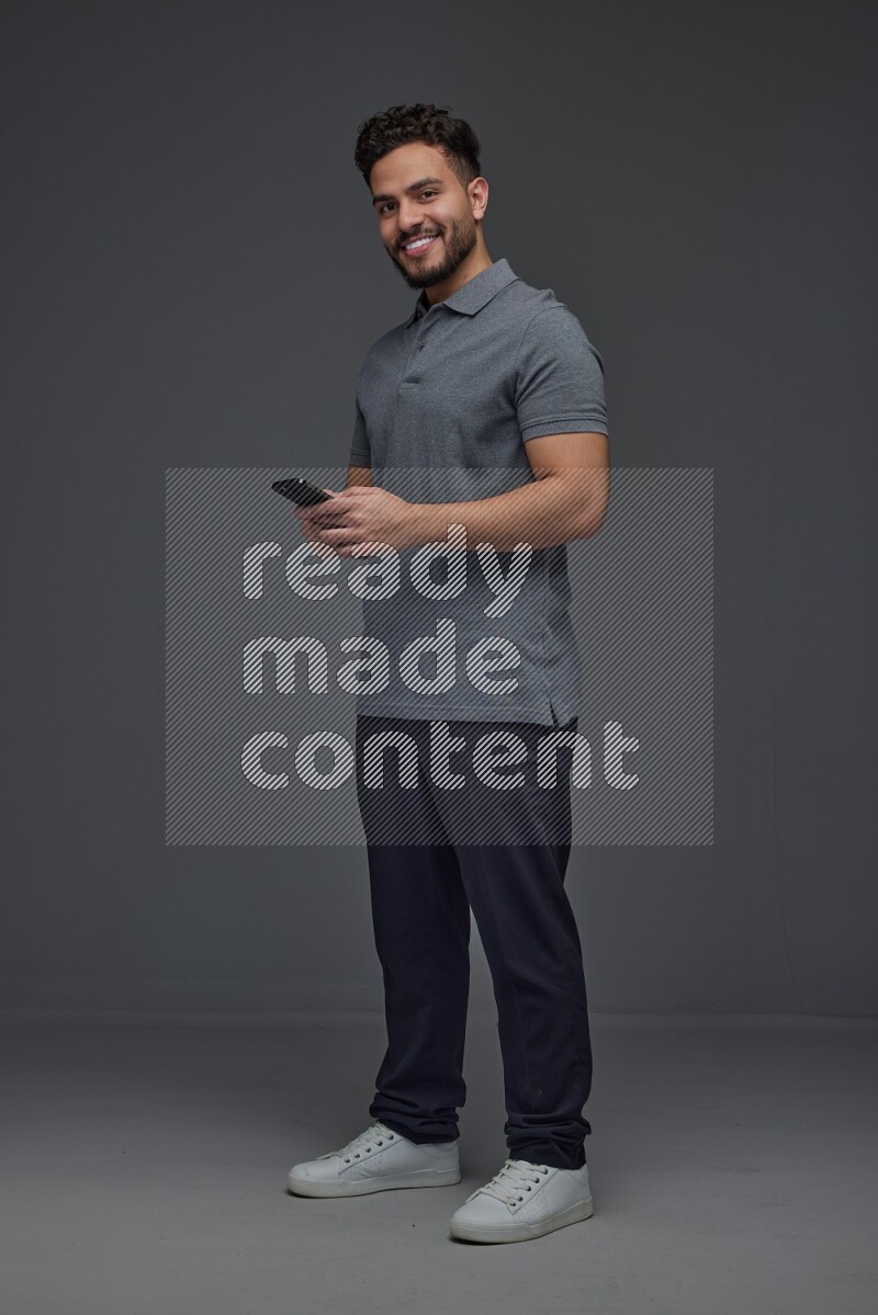 A man wearing casual standing and using his phone eye level on a gray background