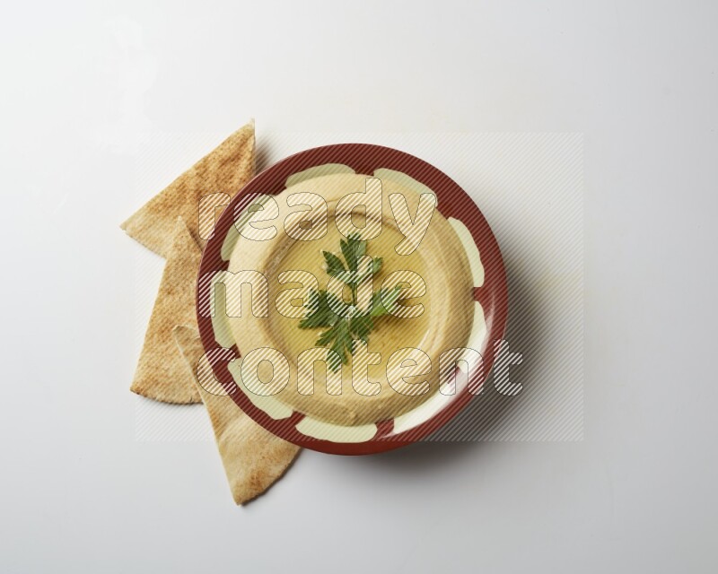 Hummus in a traditional plate garnished with parsley on a white background