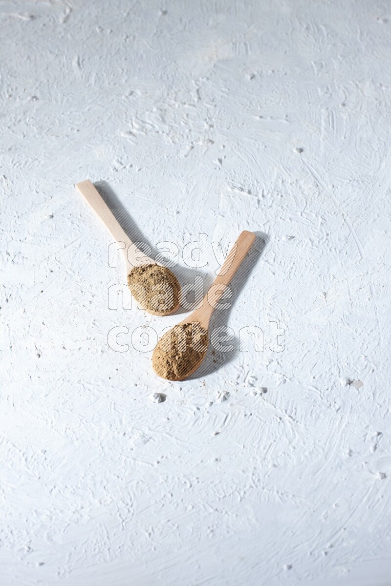 Wooden spoons full of allspice powder and allspice whole balls spreaded on a textured white flooring