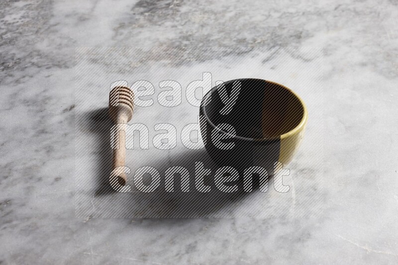 Multicolored pottery bowl with wooden honey dipper on the side on grey marble background