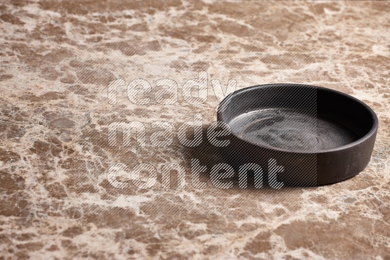 A black pottery oven plate on beige marble background