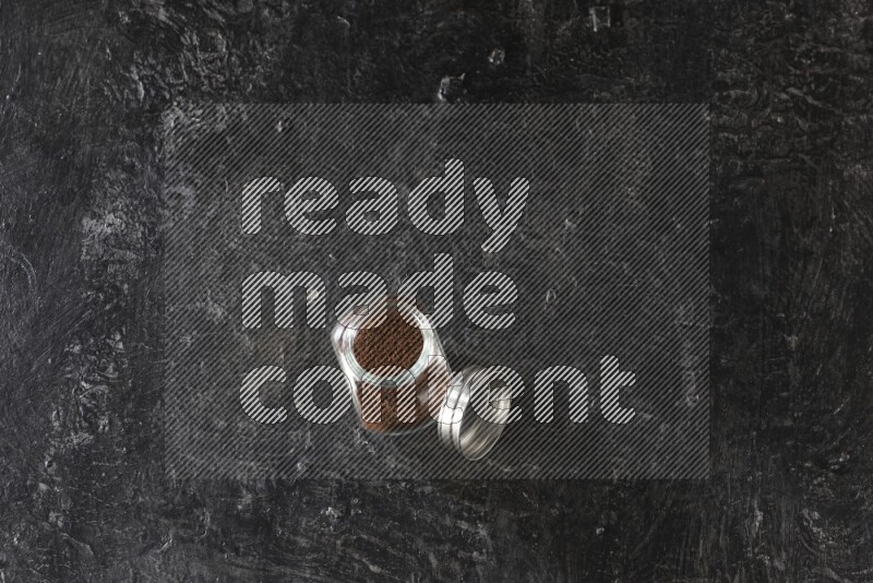 A glass spice jar full of cloves powder on textured black flooring