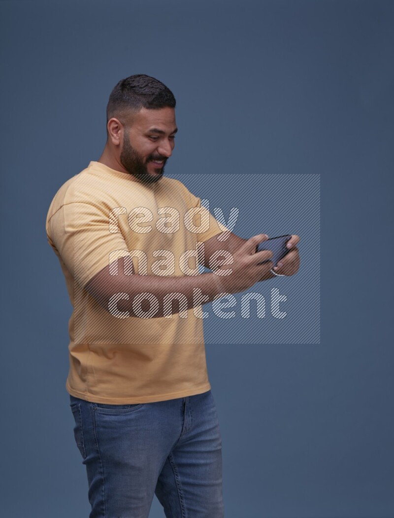 A man Playing Games on Smartphone on Blue Background wearing Orange T-shirt