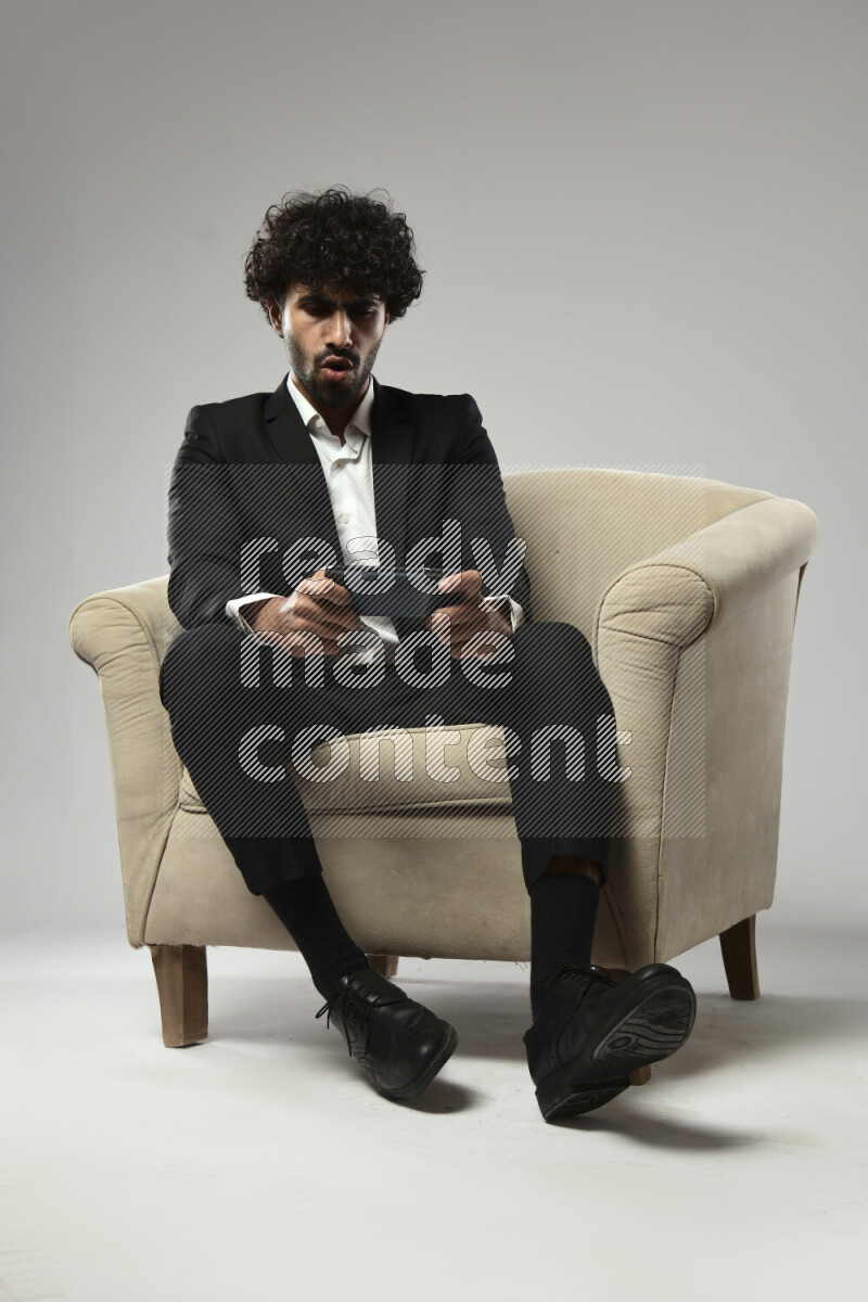 A man wearing formal sitting on a chair gaming on the phone on white background