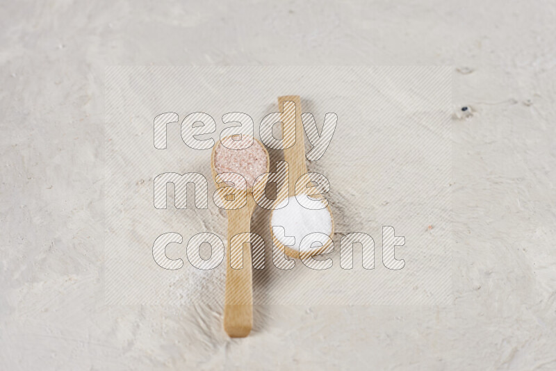 2 wooden spoons filled with fine and coarse salt on white background