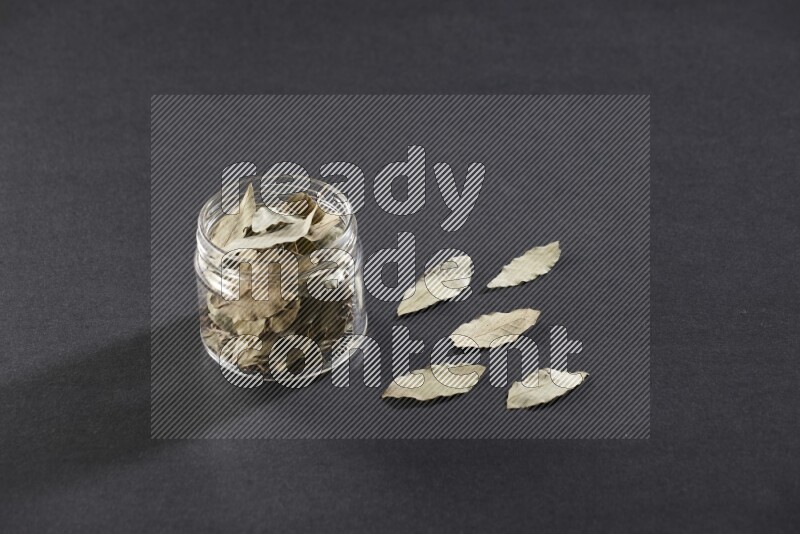 A glass jar filled with dried bay leaves on black flooring