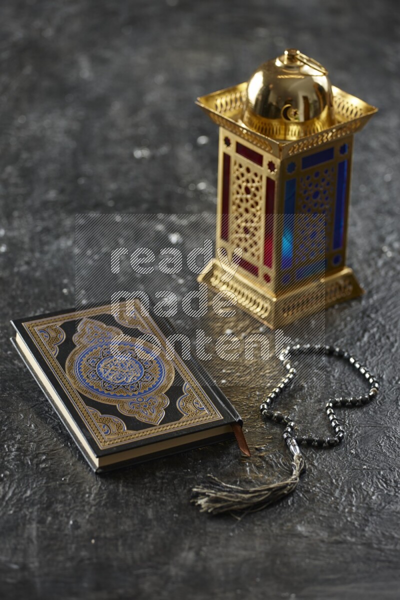 A golden lantern with different drinks, dates, nuts, prayer beads and quran on textured black background
