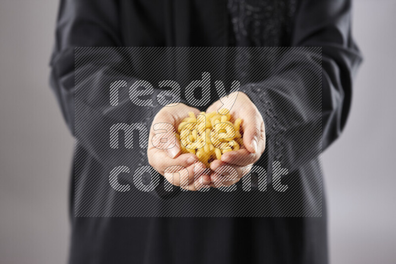Woman in abaya holding different kinds of pasta in different positions