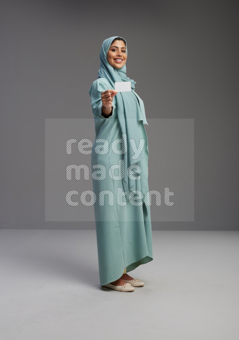 Saudi Woman wearing Abaya standing holding ATM card on Gray background