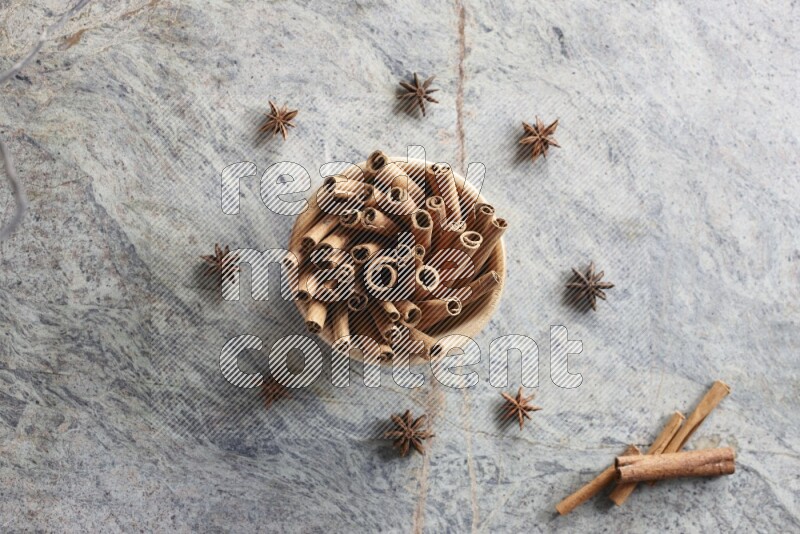 wooden bowl full of cinnamon sticks surrounded by star anis on marble background in different angles