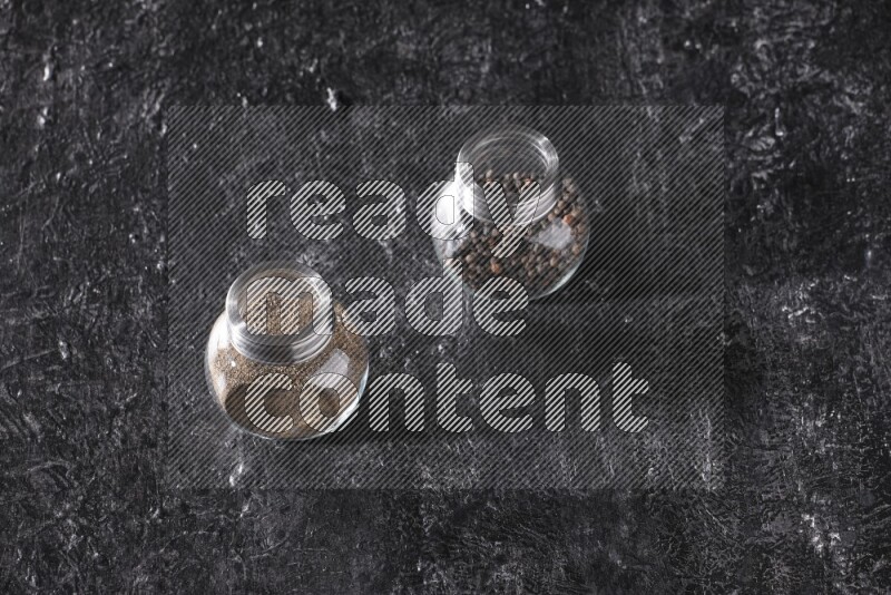 حبوب وبودرة الفلفل الأسود في أوعية زجاجية علي خلفية سوداء