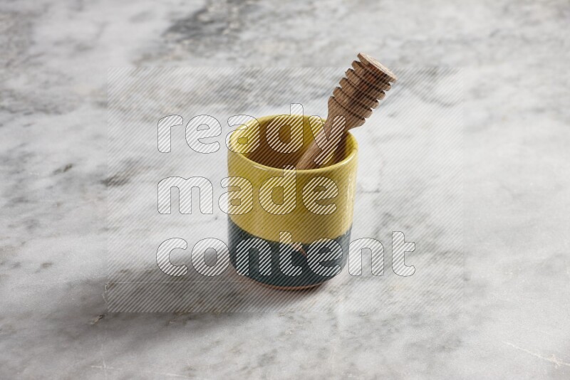 Multicolored pottery cup with wooden honey dipper in it on grey marble background