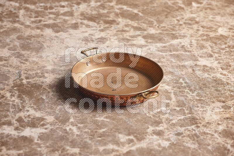 A small copper pan on beige marble background