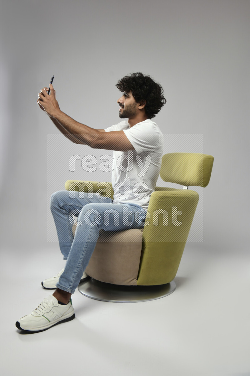 A man wearing casual sitting on a chair taking a selfie on white background