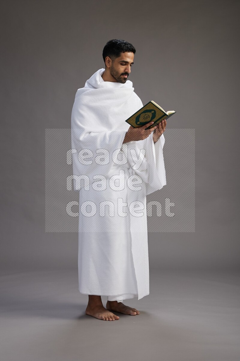 A man wearing Ehram Standing reading quran on gray background