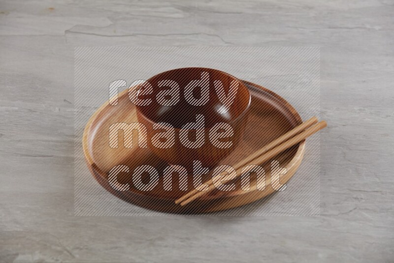 brown wood round bowl on top of brown wood round plate and wood chopsticks, on grey textured countertop