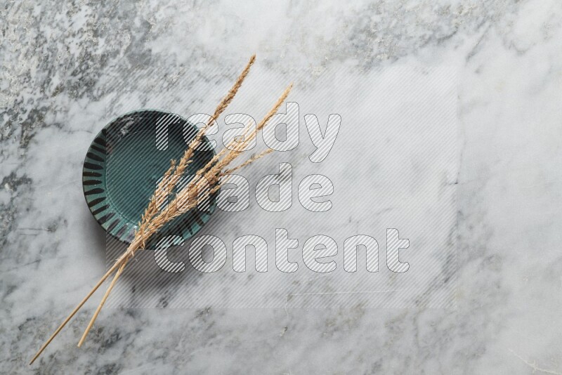 Wheat stalks on multicolored pottery plate on grey marble background