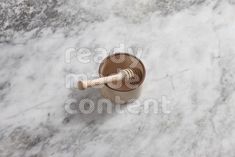 Beige Pottery oven bowl with wooden honey handle on the side with grey marble flooring, 65 degree angle