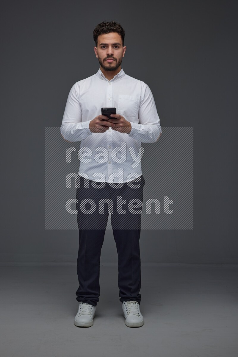 A man wearing smart casual standing and using his phone eye level on a gray background