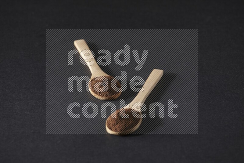 2 wooden spoons full of cloves powder on a black flooring