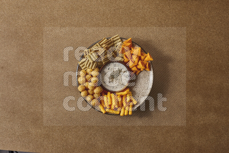Assorted snacks on a pottery plate with a dipping on brown background
