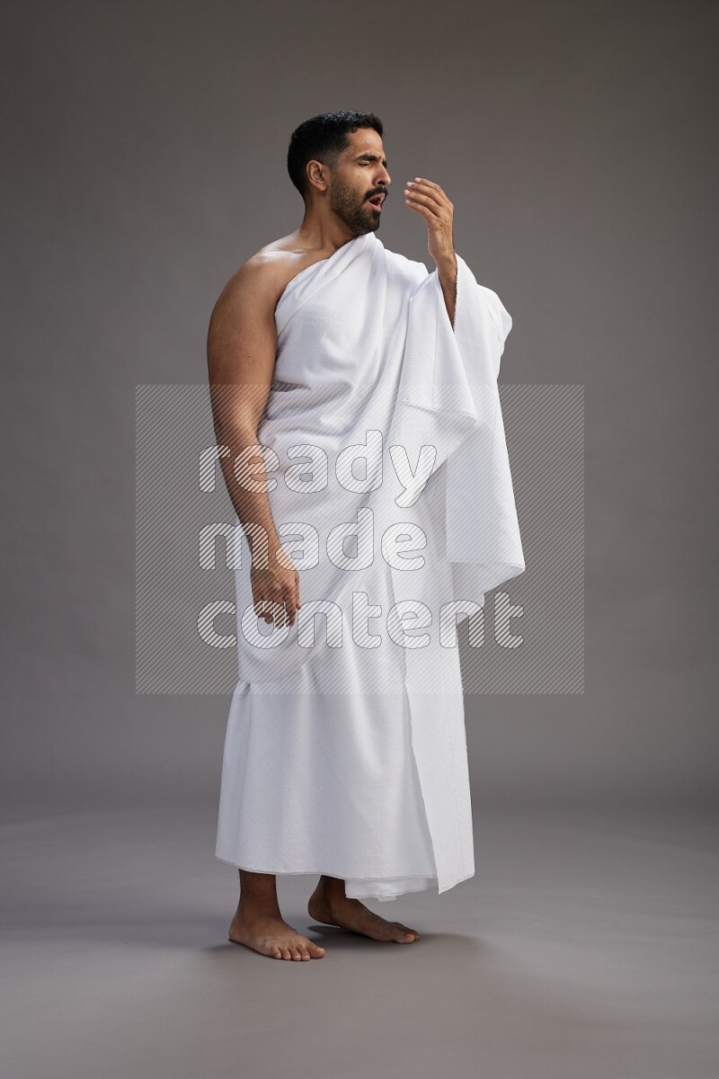 A man wearing Ehram standing showing how to sneeze on gray background
