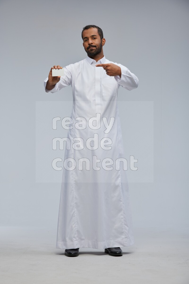Saudi man wearing Thob standing holding ATM card on Gray background