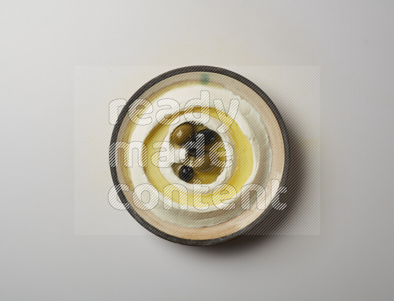 Lebnah garnished with whole black olives in a pottery plate on a white background