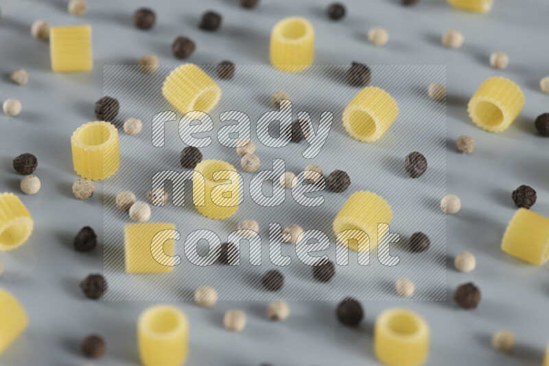 Raw pasta with different ingredients such as cherry tomatoes, garlic, onions, red chilis, black pepper, white pepper, bay laurel leaves, rosemary, cardamom and mushrooms on light blue background