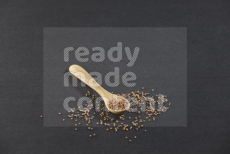 A wooden spoon full of mustard seeds on a black flooring