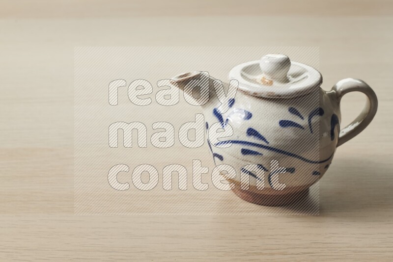 A pottery teapot on light wooden background