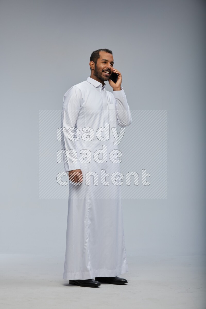 Saudi man wearing Thob standing talking on phone on Gray background
