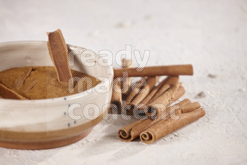 Ceramic bowl full of cinnamon powder with cinnamon sticks on the side on white background