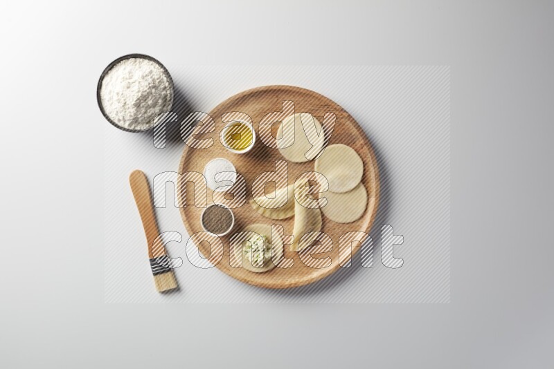 two closed sambosas and one open sambosa filled with cheese while flour, salt, black pepper and oil with oil brush aside in a wooden dish on a white background