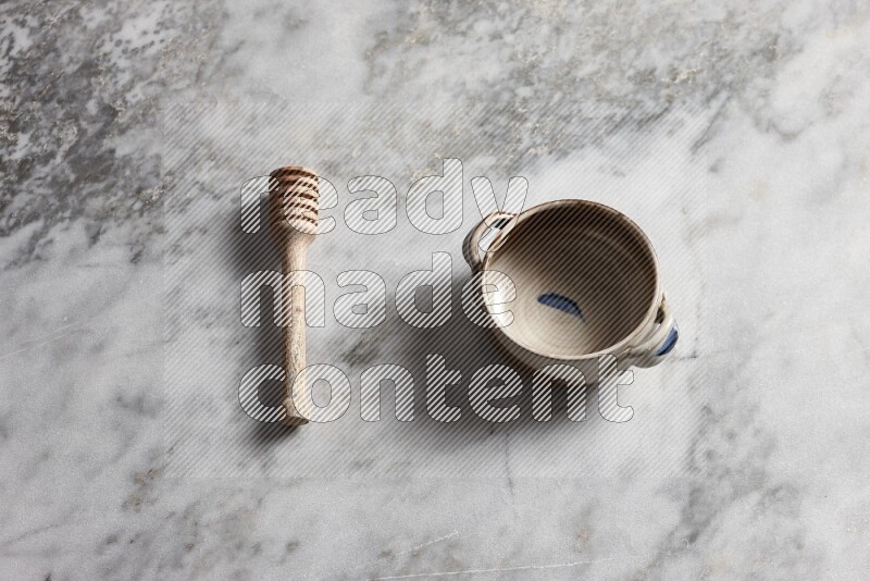 Multicolored pottery bowl with wooden honey dipper on the side on grey marble background
