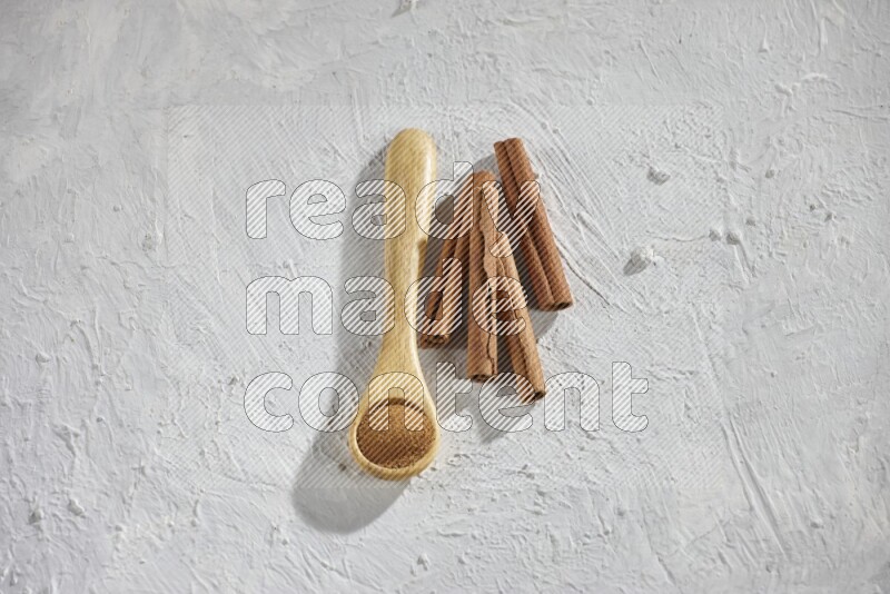 Cinnamon powder in a wooden spoon with cinnamon sticks on white background