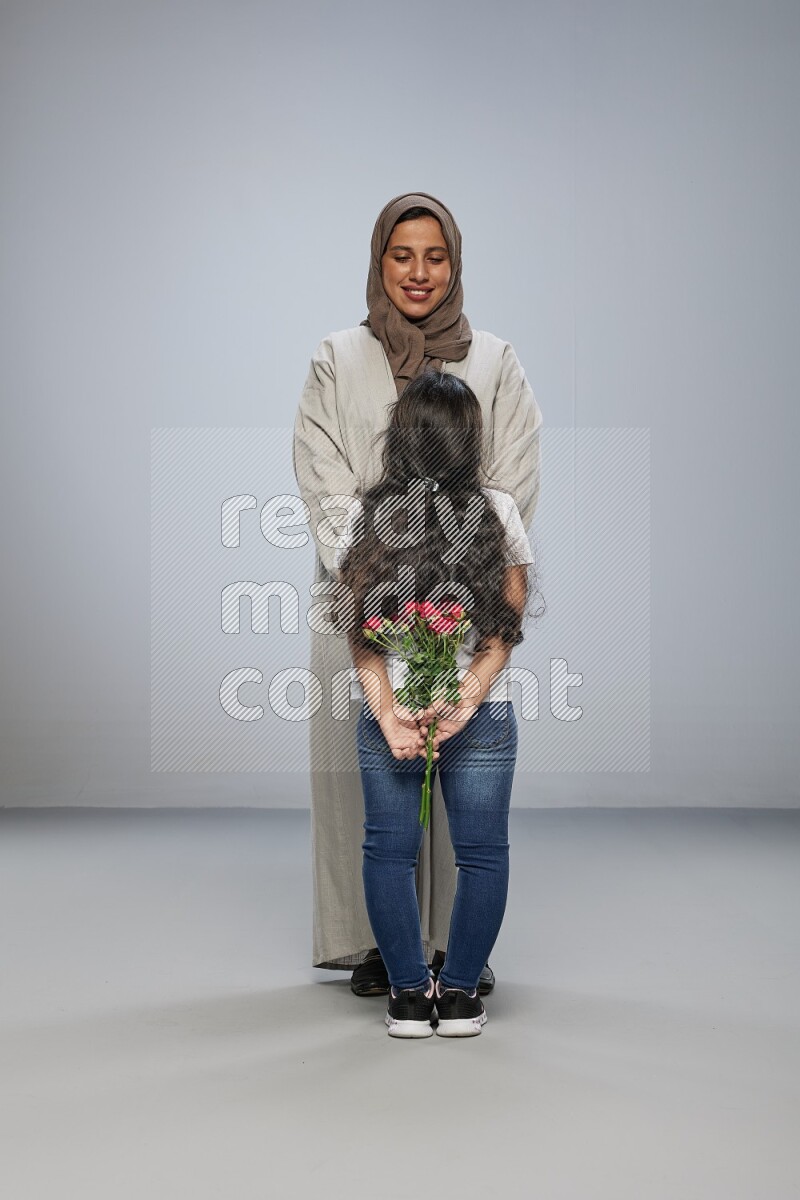 A girl hiding a flower behind her back for her mother on gray background