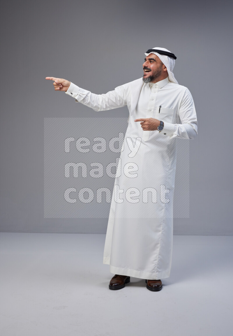 Saudi man Wearing Thob and white Shomag standing interacting with the camera on Gray background