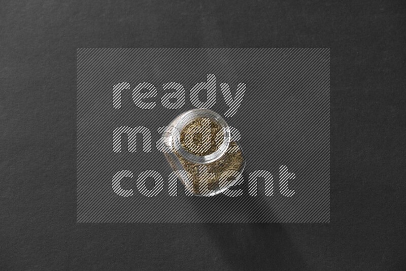 A glass spice jar full of cumin on black flooring