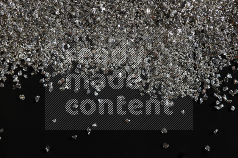 Silver shimmering fragments of glass scattered on a black background